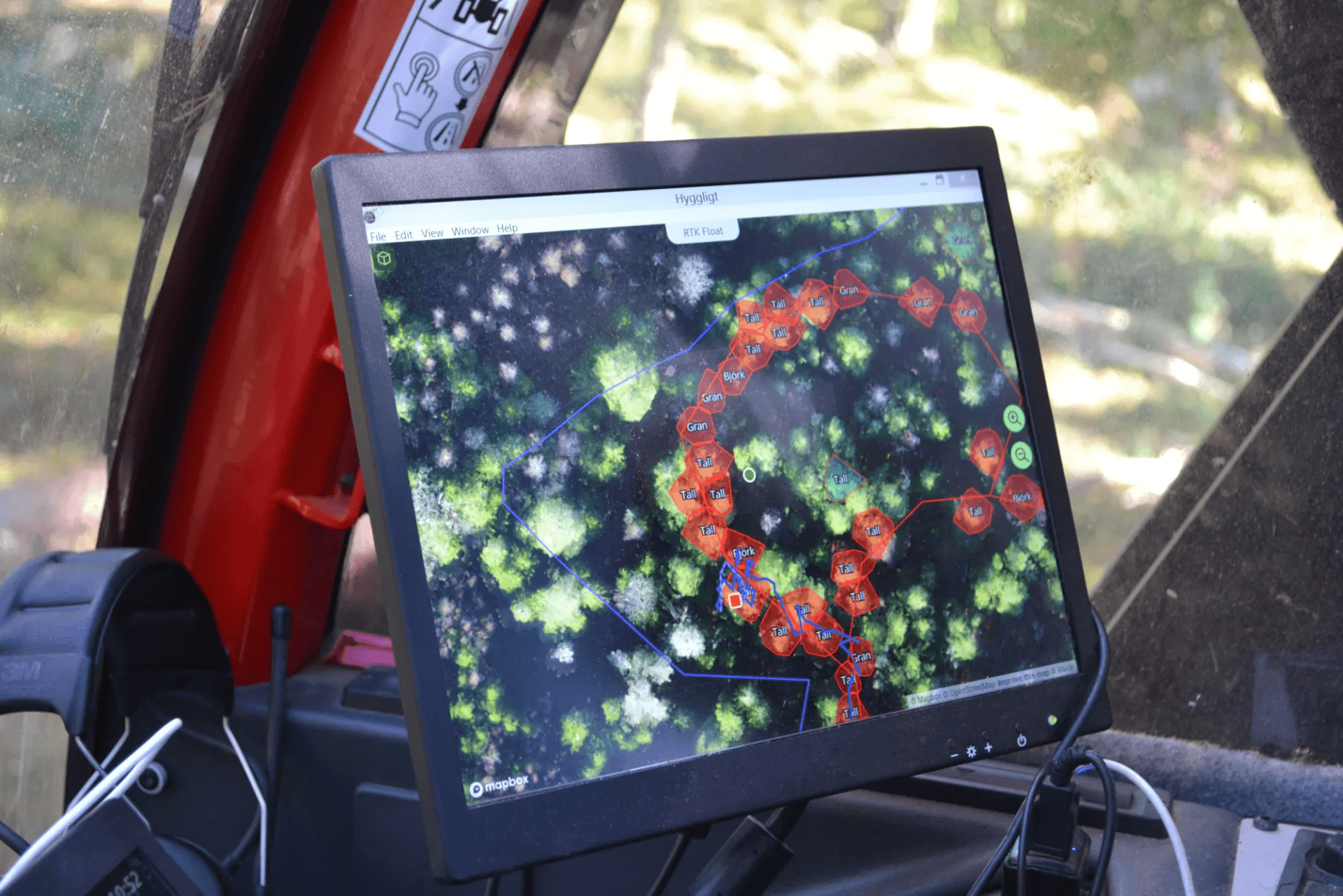 Skärm som visar en karta över skog med markerade träd och rutter. Monterad på instrumentbrädan i en skördare (skogsmaskin).