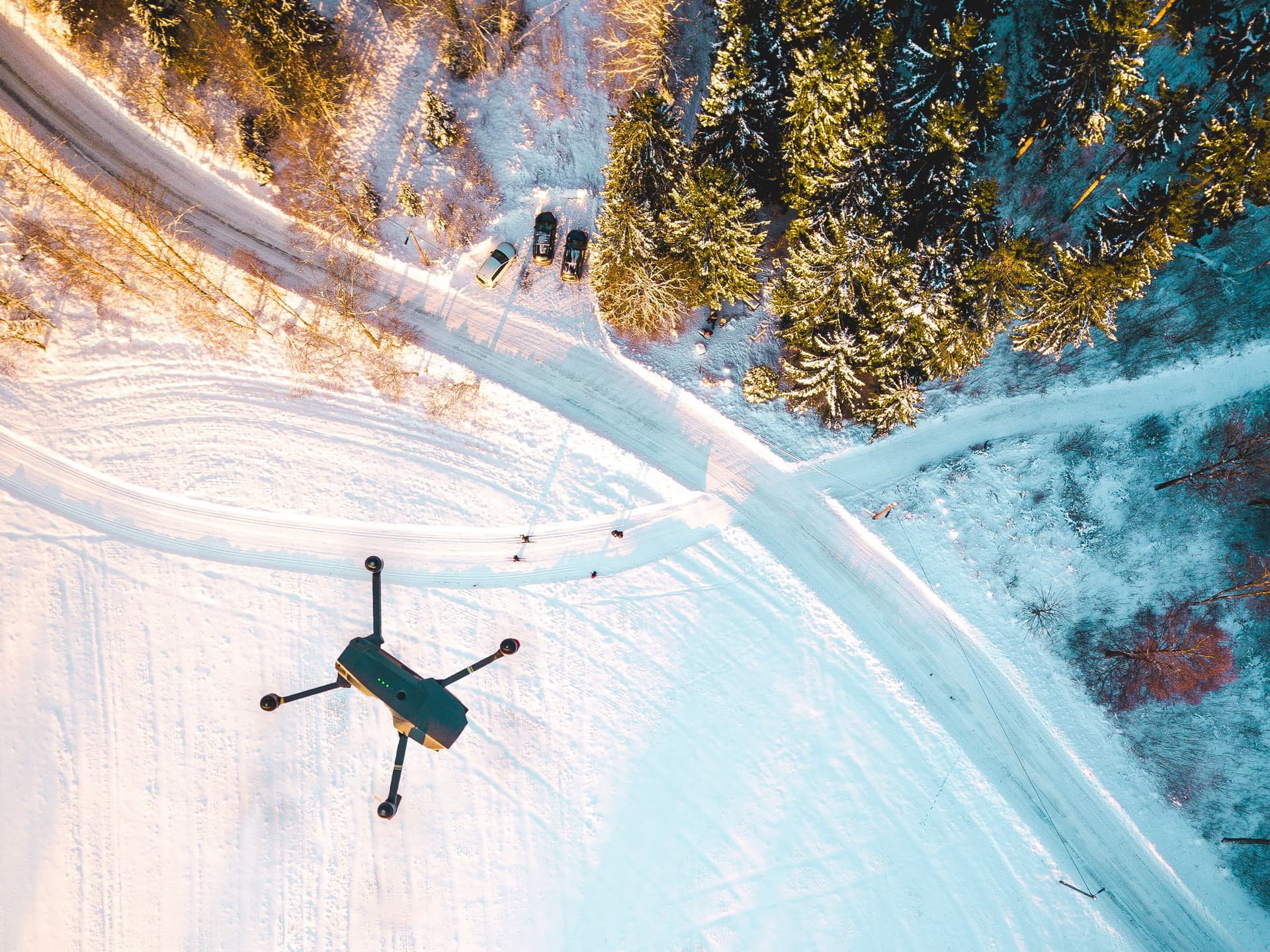 Drönare flyger över en snötäckt skogsväg med tre parkerade bilar.