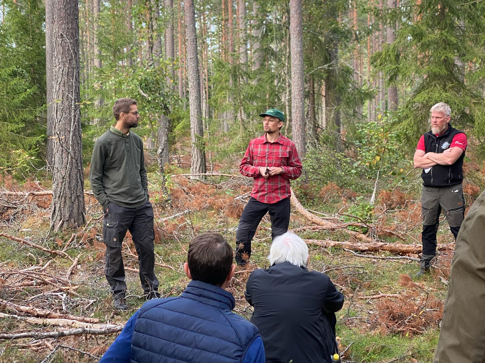 Grupp i skogen, en person i röd rutig skjorta pratar med en grupp människor.